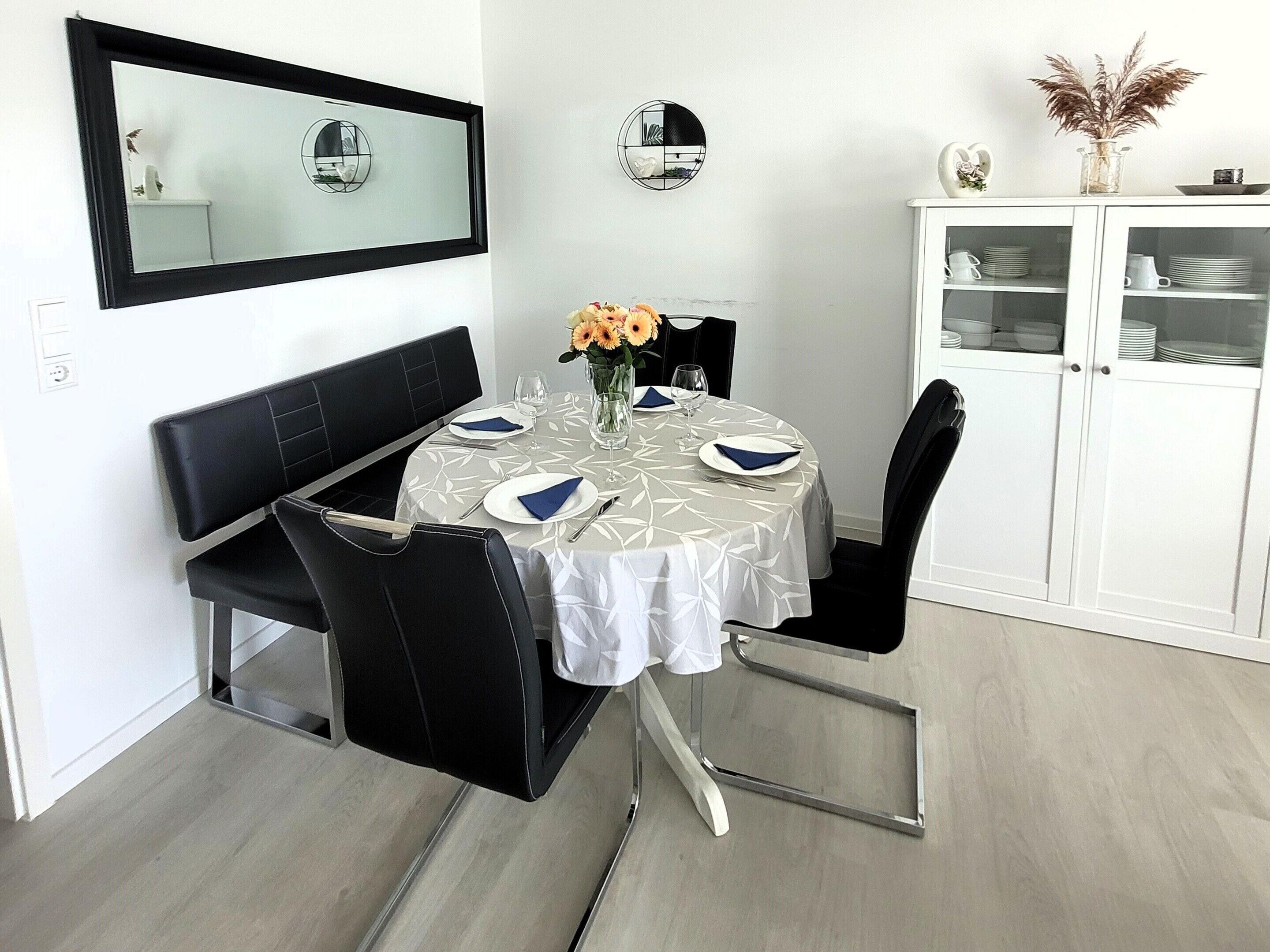 A dining area with a round table, black chairs, a white cabinet with glass doors, and a wall-mounted mirror.