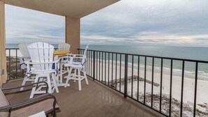 A balcony with white Adirondack chairs and a table, overlooking a sandy beach and ocean. - Phoenix I 1078 3 Bedroom Condo (Orange Beach)