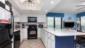 A modern kitchen with white cabinets, a black refrigerator, a microwave, and an oven. There is a large window providing a view of the ocean. - Phoenix I 1078 3 Bedroom Condo (Orange Beach)