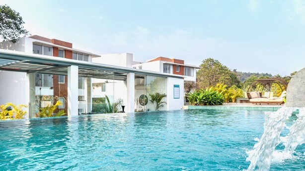 A modern hotel with a swimming pool, outdoor seating, and a waterfall feature. - Modern 2bhk w Pool Access 5km to Coco Beach (Nerul)