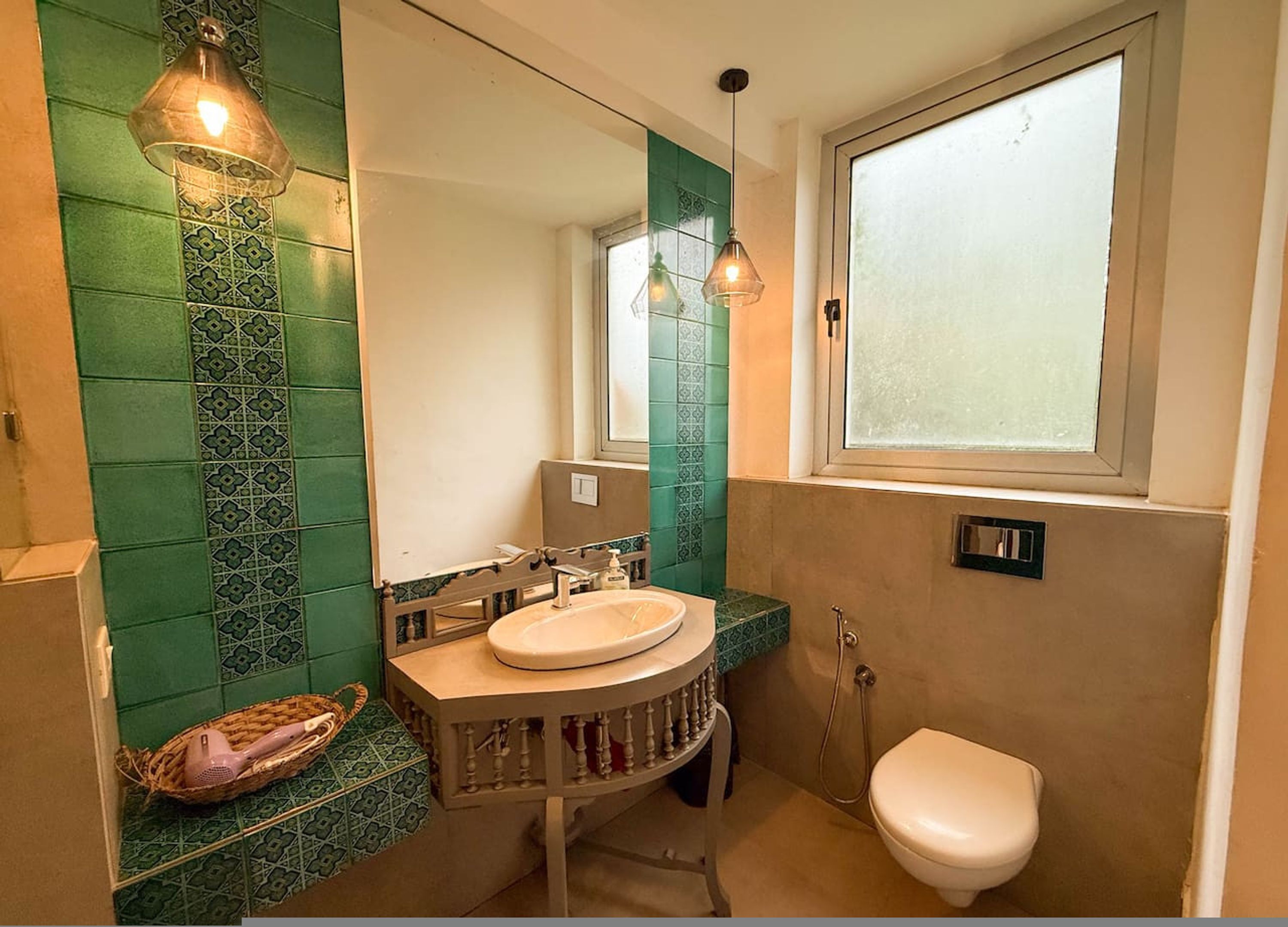Un baño con pared de azulejos verdes, un lavabo redondo, un espejo, una ventana y un inodoro.