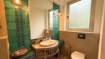 Un baño con pared de azulejos verdes, un lavabo redondo, un espejo, una ventana y un inodoro.