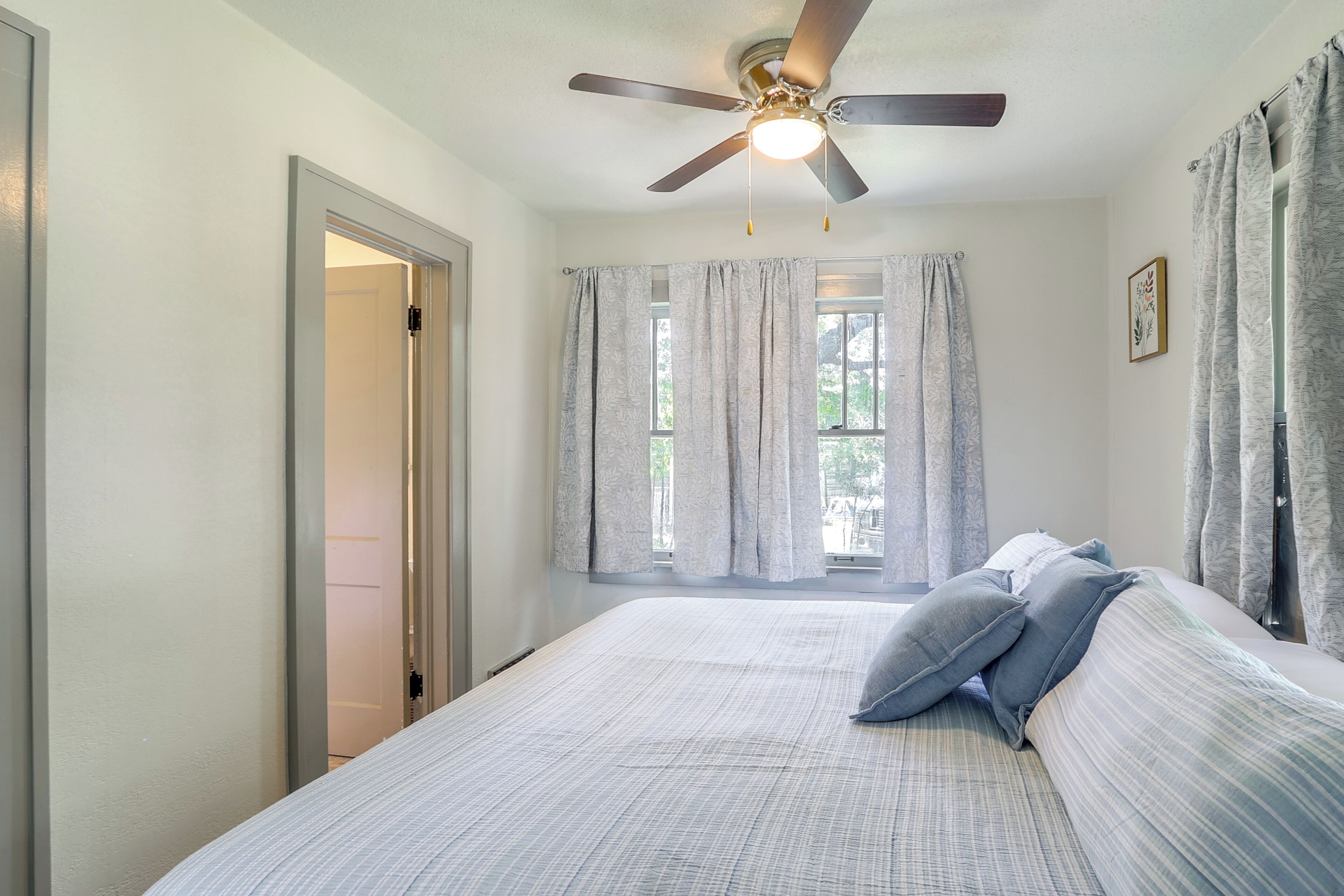 Un dormitorio con cama, ventilador de techo, ventana con cortinas y puerta.