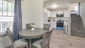 A modern kitchen with white cabinets, a stainless steel refrigerator, and a microwave. There is a dining area with a round table and chairs, and a staircase leading to an upper level. - 4 Mi to Dtwn: Charming Retreat in Wichita! (Wichita)
