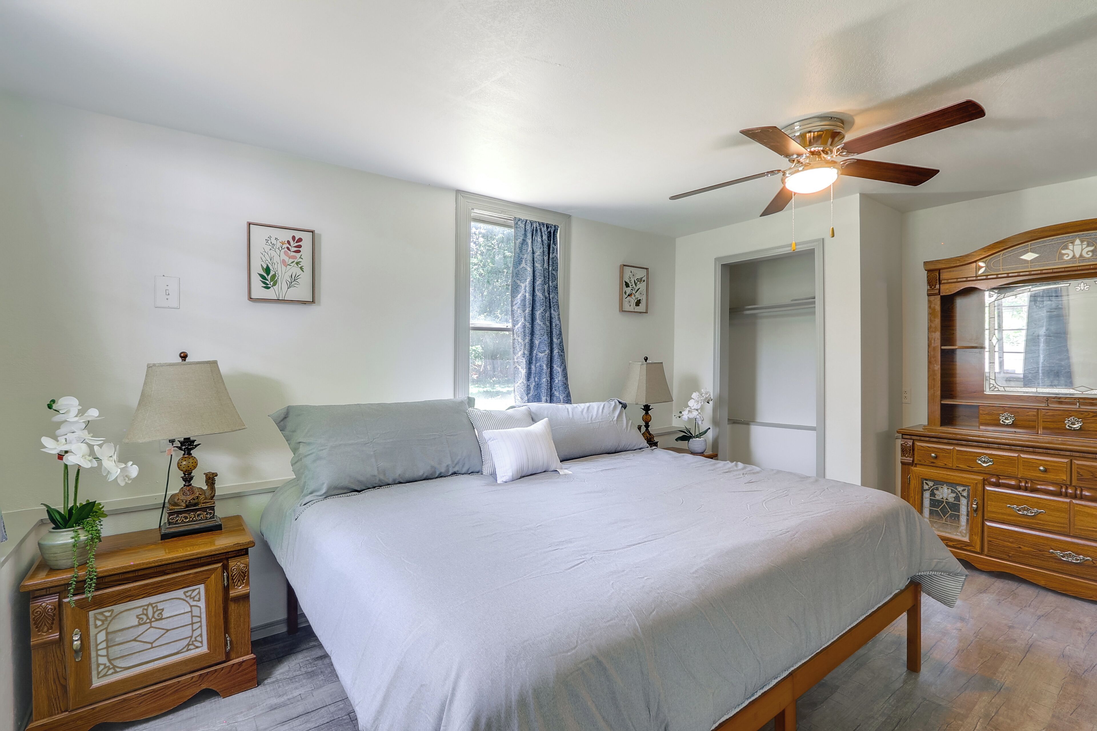 A bedroom with a bed, nightstands, a dresser, a ceiling fan, and a window with curtains.