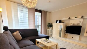 A modern living room with a sofa, a coffee table, a TV mounted on the wall, and a decorative ceiling light. - Apartment in Winterberg Near Ski Lifts (Winterberg)