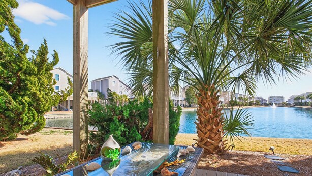 A glass-top table with seashells and a decorative vase, surrounded by palm trees and a wooden deck. - 5BR/4BA Sleeps 10 w/ Community Pools & Short Beach Walk (Ocean Isle Beach)