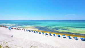 Ein Strand mit weißem Sand, klarem türkisblauem Wasser und blauen Sonnenschirmen.