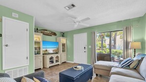 A living room with a television, a ceiling fan, and a view of the outdoors.