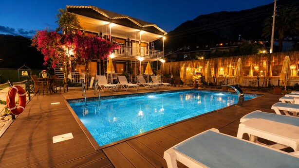 A swimming pool with lounge chairs, a lifebuoy, and a building with a balcony and outdoor seating area. - Fİİ SUİTS (Kumluca)