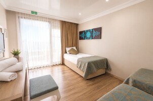 Une chambre d’hôtel avec un lit, un banc, une petite table avec des serviettes, un tableau au mur et une fenêtre avec des rideaux.