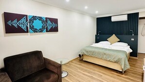 A modern bedroom with a bed, a brown sofa, and a wall-mounted air conditioner. - Fİİ SUİTS (Kumluca)