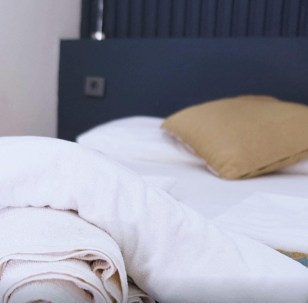 A neatly made bed with a white and beige pillow, a folded white blanket, and a dark headboard.