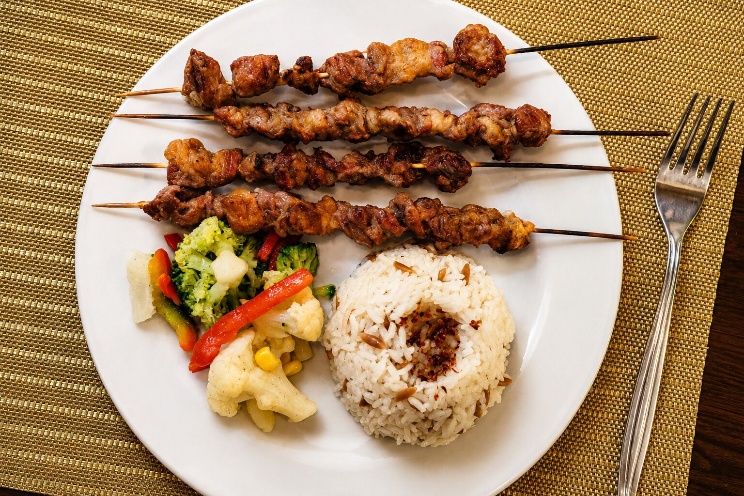 Une assiette contenant des brochettes, du riz et des légumes variés.