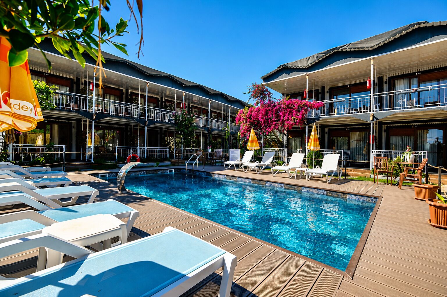 A swimming pool with lounge chairs, a lifeguard stand, and a building with balconies.
