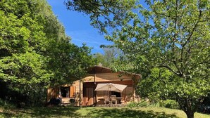 Een houten hut met een terras, omgeven door weelderige begroeiing.