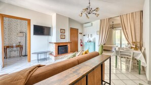 A living room with a fireplace, a sofa, a dining table with chairs, and a kitchen area in the background. - Umbria Casa Vacanze – Panoramic Views & Relaxation Near Marmore Falls (Montefranco)