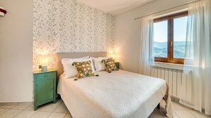 A bedroom with a bed, two pillows, a nightstand, a window with curtains, and a view of the outdoors. - Umbria Casa Vacanze – Panoramic Views & Relaxation Near Marmore Falls (Montefranco)