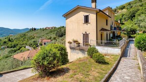 A hillside house with a paved pathway, a small balcony with potted plants, and a view of the surrounding hills. - Umbria Casa Vacanze – Panoramic Views & Relaxation Near Marmore Falls (Montefranco)