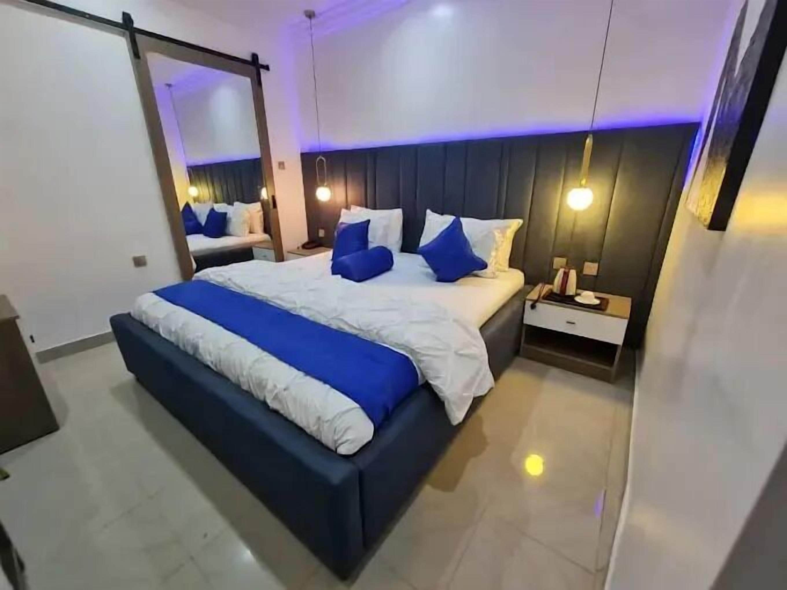 Une chambre moderne avec un grand lit, des tables de chevet, un miroir et un éclairage d’ambiance.