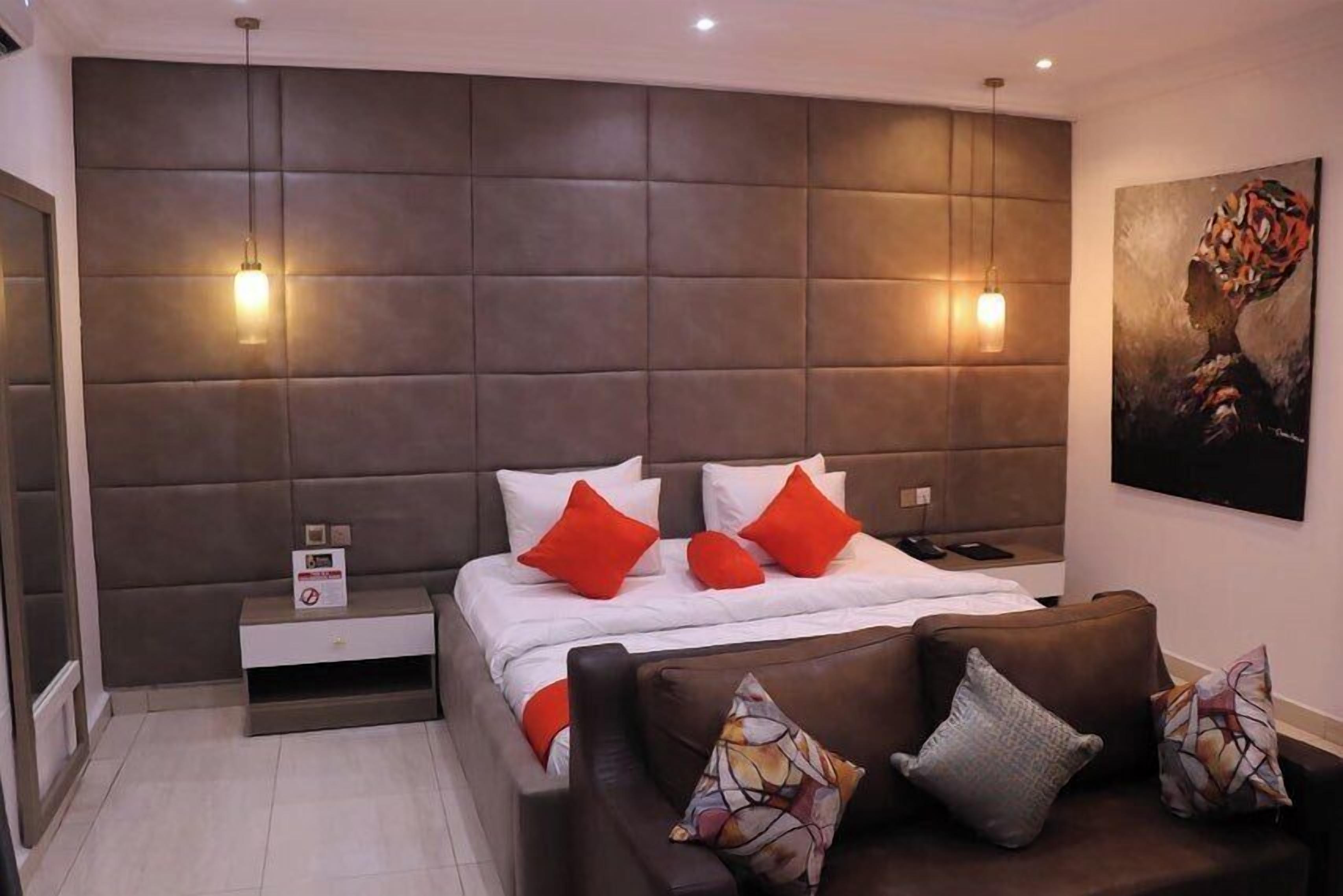 A modern bedroom with a large bed, two bedside tables, a sofa, and a painting on the wall.