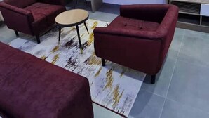 Een moderne woonkamer met een flatscreen televisie aan de muur, twee rode banken, een klein rond tafeltje en een tapijt met een patroon.