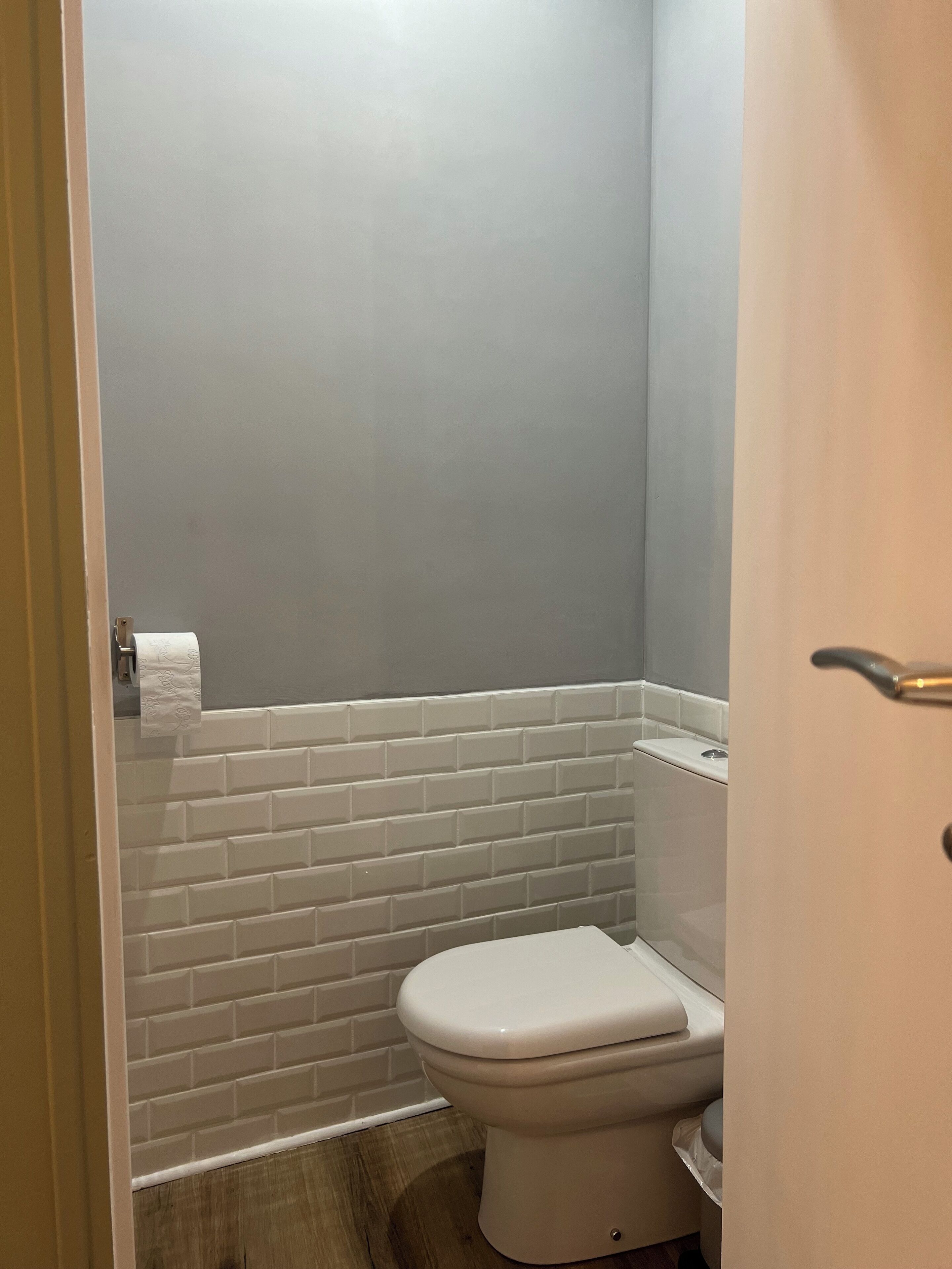 Een kleine badkamer met toilet, witte betegelde wanden en een houten vloer.
