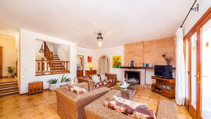 Una sala de estar con muebles de mimbre, chimenea, televisor y escalera.
