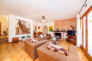 A living room with wicker furniture, a fireplace, a television, and a staircase.