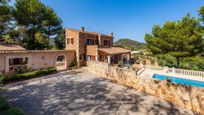 Una casa de dos pisos con un muro de piedra y una piscina.