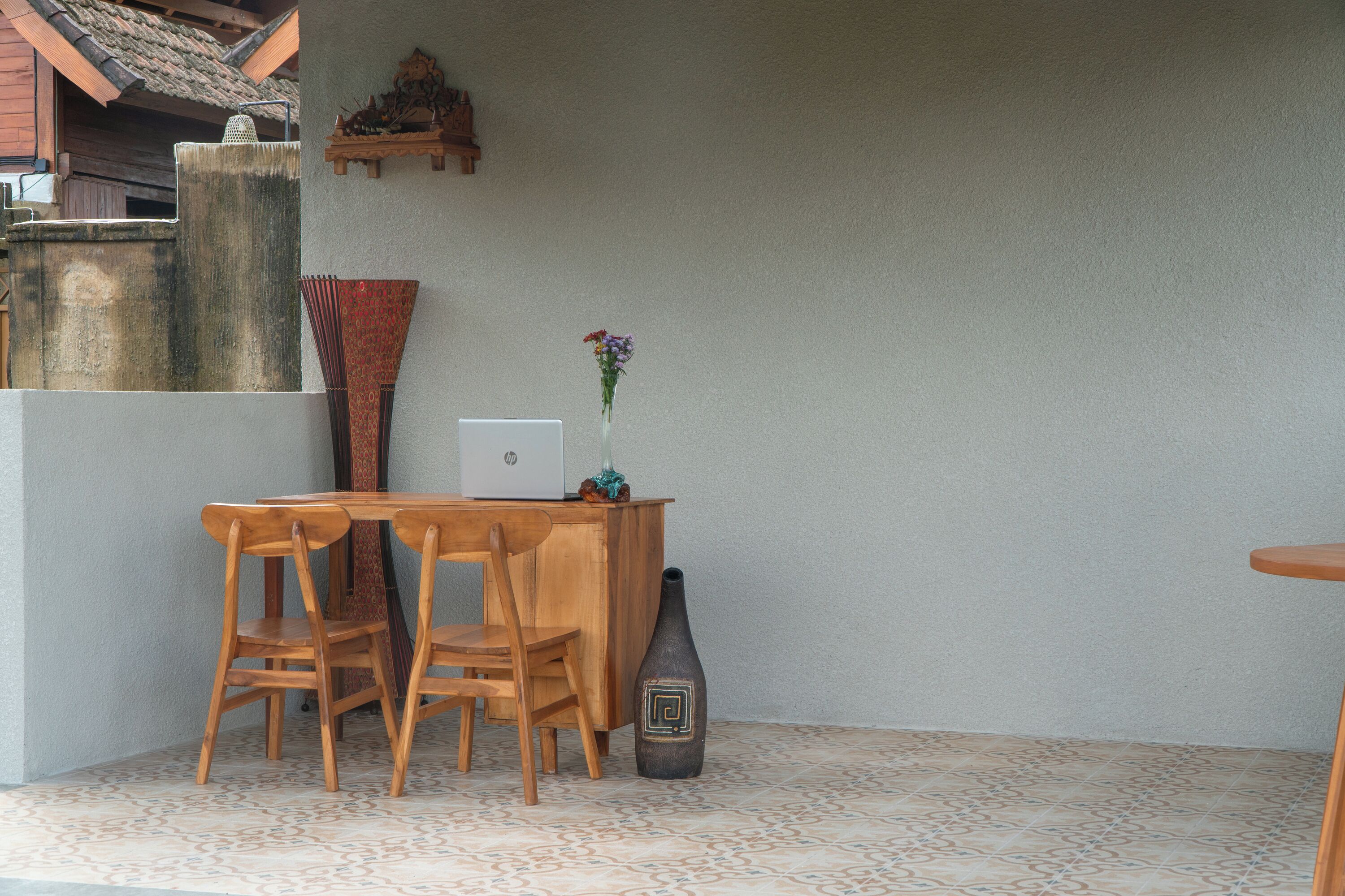 A wooden dining table with chairs, a vase with flowers, and a decorative vase on the wall.