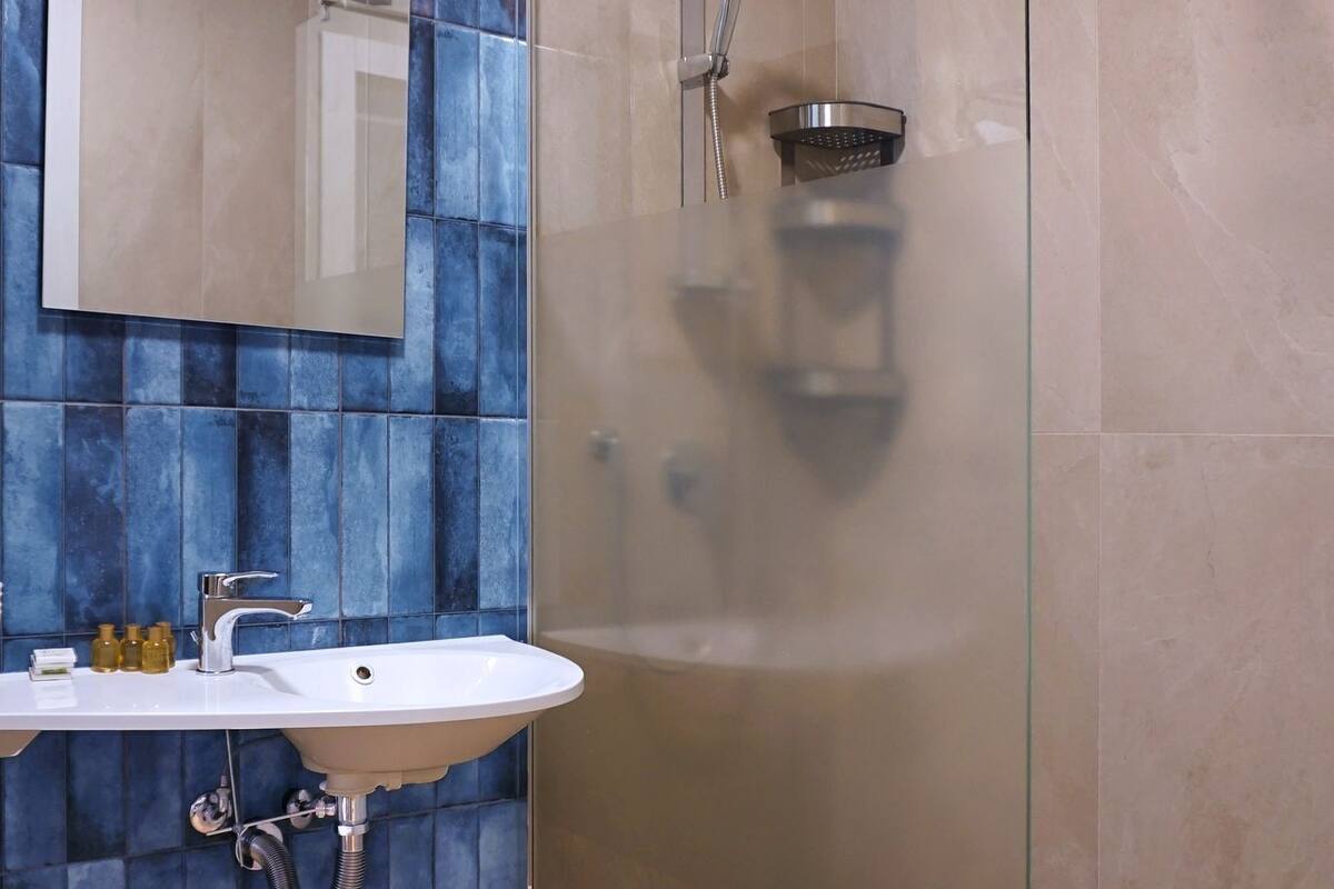 A modern bathroom with a glass-enclosed shower, a white sink with a mirror above it, and blue-tiled walls.