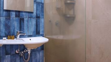 A modern bathroom with a glass-enclosed shower, a white sink with a mirror above it, and blue-tiled walls.