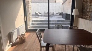 A room with a wooden floor, a dark wooden table, and chairs. There is a large sliding glass door leading to an outdoor area with a stone wall and outdoor furniture. - City Victorian Townhouse Cork, Kennedy Park (Cork)