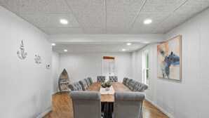 Un salón de conferencias con una larga mesa de madera, sillas tapizadas en gris, paredes de ladrillo blanco e iluminación empotrada en el techo.