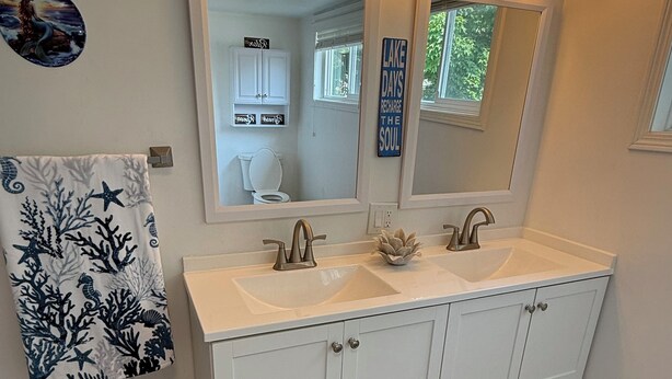 Un baño con lavamanos doble, armarios blancos, un espejo grande y una toalla decorativa.