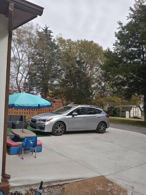 A silver car parked in a driveway with a blue umbrella and outdoor furniture in the background. - Relax Farm house - Self check in /WIFI -Tiny House (Murfreesboro)