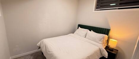 A bedroom with a bed, a nightstand, a lamp, and a ceiling vent.