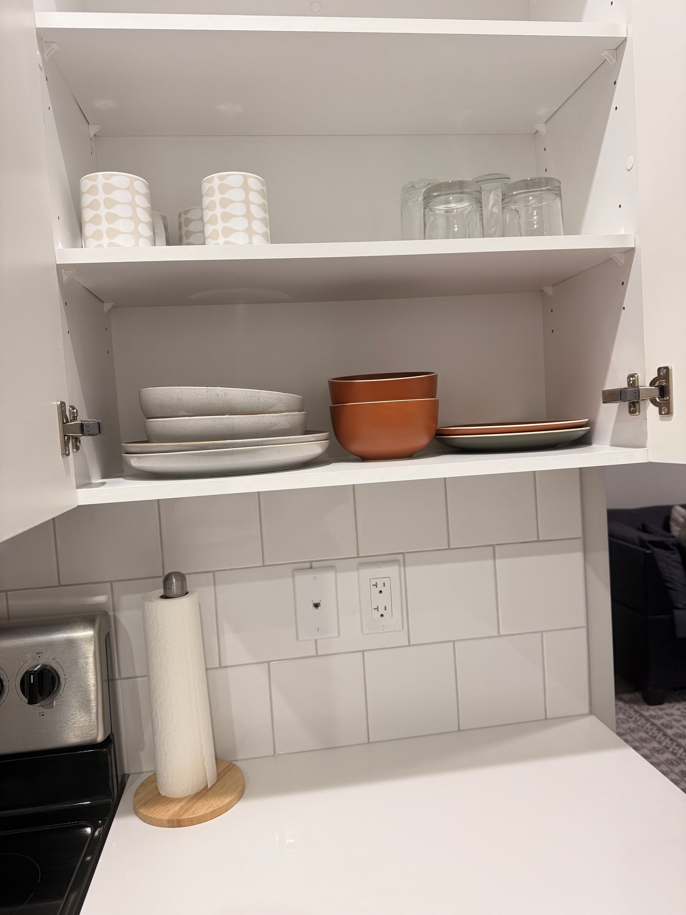 A kitchen with white cabinets, a stove, and a countertop. There are plates, bowls, and a roll of paper towels on the counter.