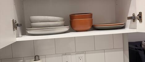 A kitchen with white cabinets, a stove, and a countertop. There are plates, bowls, and a roll of paper towels on the counter.