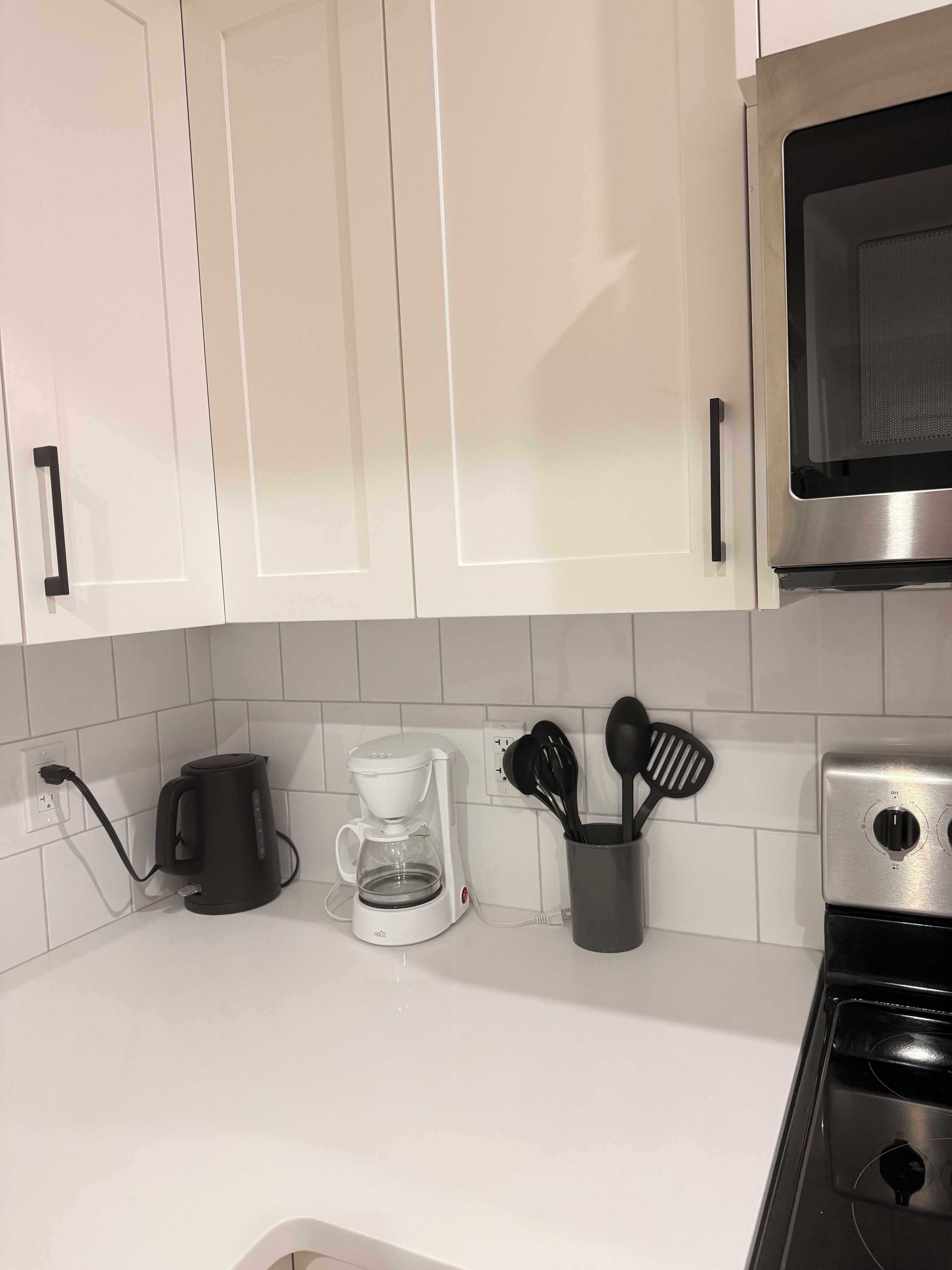 A kitchen with white cabinets, a coffee maker, a kettle, and a stove.