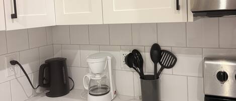 A kitchen with white cabinets, a coffee maker, a kettle, and a stove.