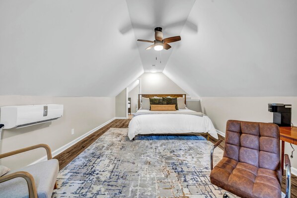 Un dormitorio con cama, ventilador de techo, piso de madera y alfombra estampada.