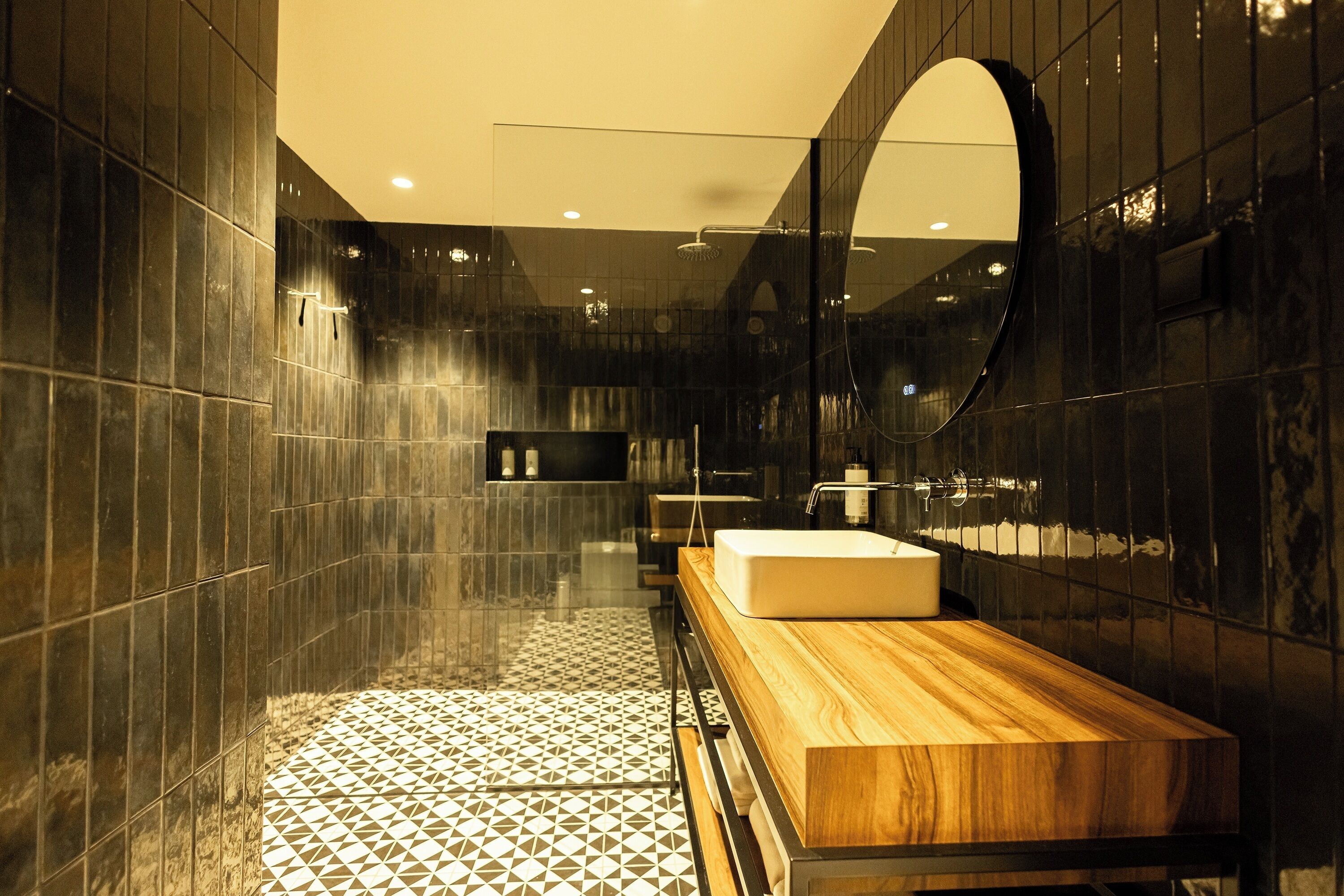 A modern bathroom with a large mirror, a wooden vanity, and a geometric patterned floor.