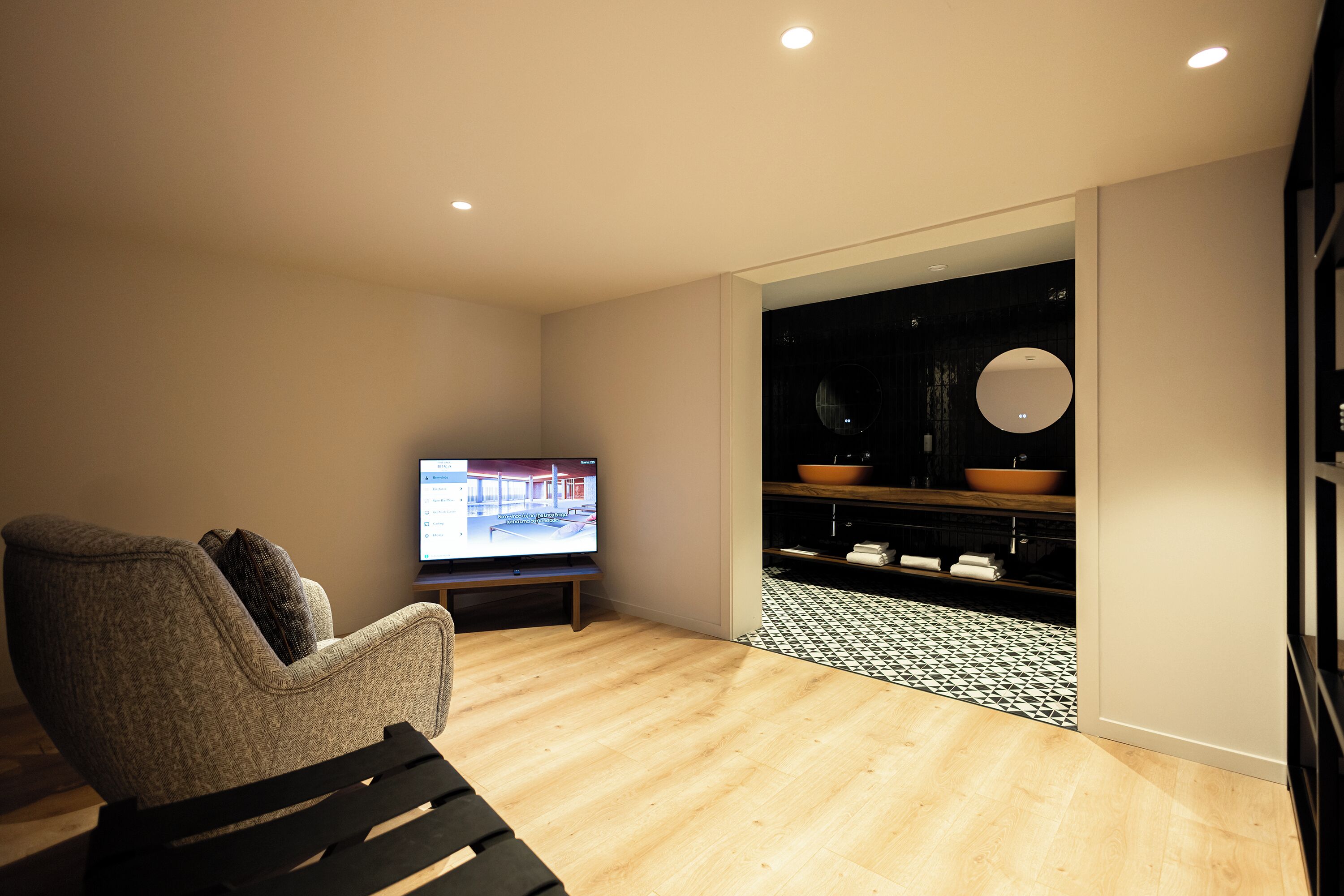 Una sala de estar moderna con televisor, sofá, piso de madera y área de cocina con salpicadero de azulejos blanco y negro.