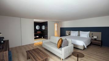 Una camera d'hotel moderna con un divano, un letto, un tavolino in legno e un piccolo comodino.