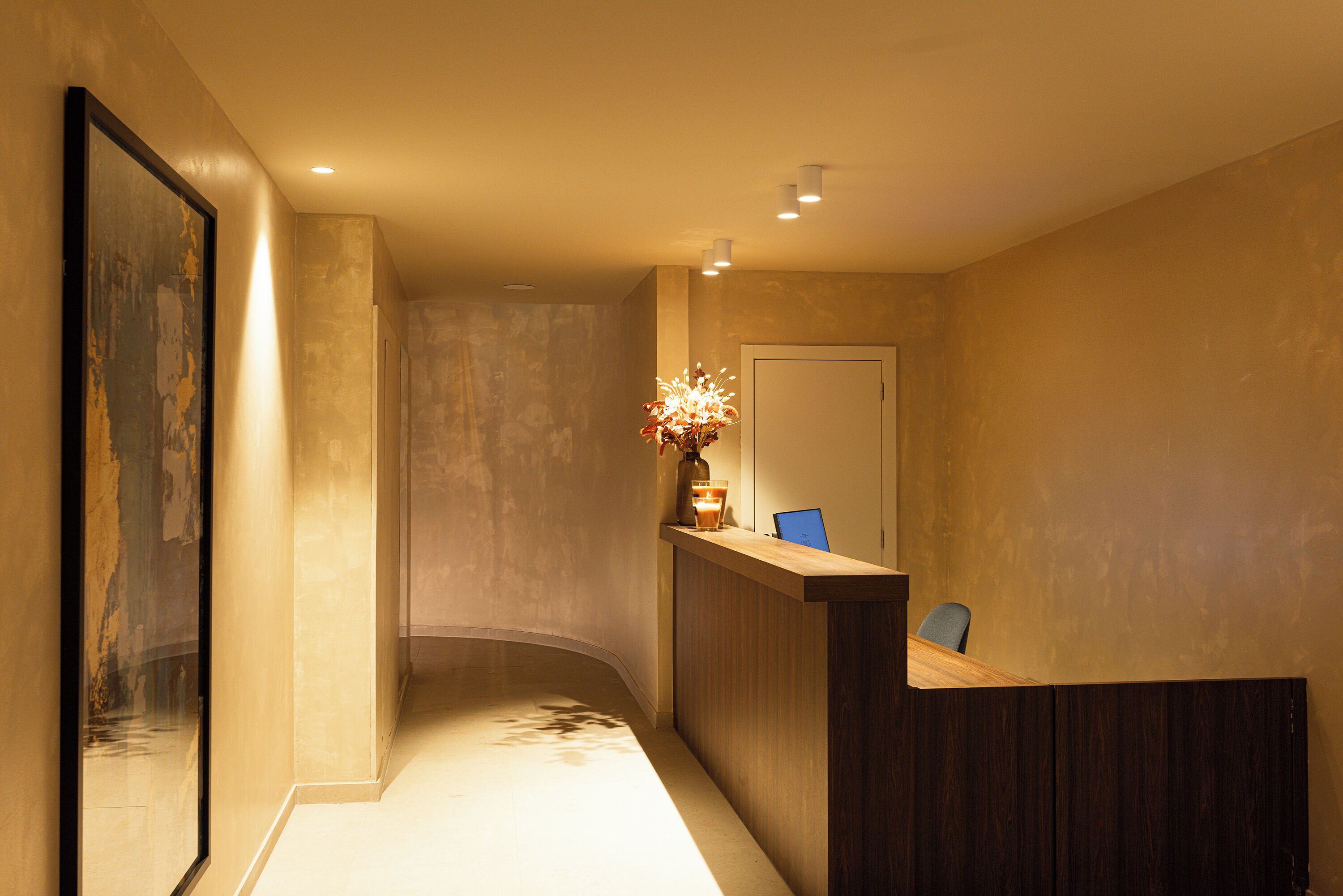 A reception area with a wooden counter, a vase with flowers, and a chair.