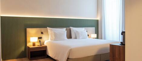 A modern hotel room with a neatly made bed, a wooden nightstand with a lamp, a small table, and a green accent wall.