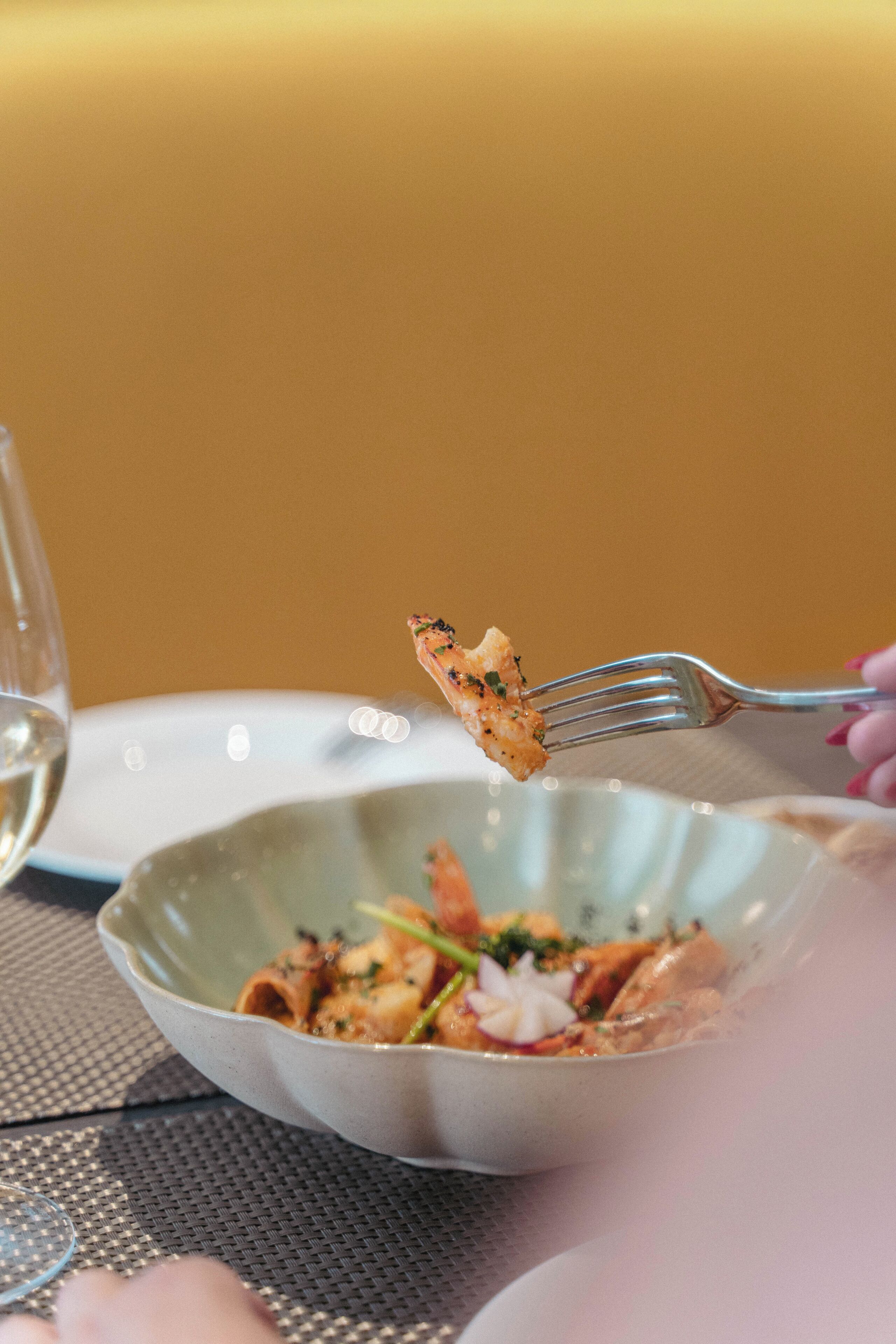 A dining table with a bowl of pasta and a fork.
