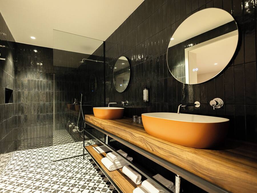 Un baño moderno con dos lavamanos ovalados, un mueble de tocador de madera y un espejo grande.